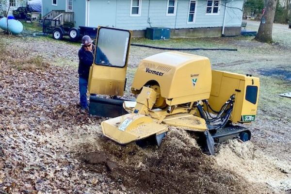 Machinery being used for stump removal in garden by house.